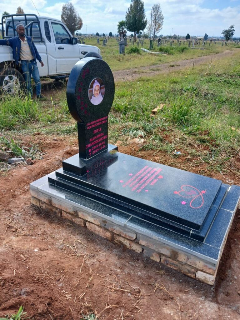 Side view of black granite baby tombstone and grave cover with pink engravings at South Park Cemetery Germiston